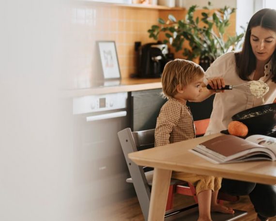 A mom and her child baking in a cozy kitchen surrounded by pumpkins.